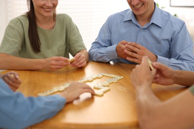 Photo of Happy friends playing dominoes at wooden table indoors, closeup