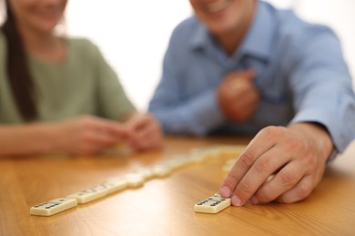 Photo of Friends playing dominoes at wooden table against light background, closeup
