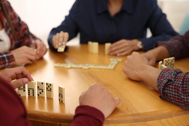 Photo of Friends playing dominoes at wooden table against light background, closeup