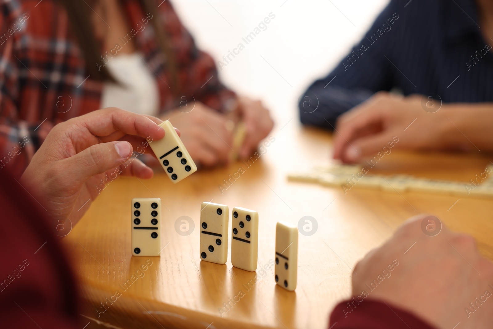 Friends playing dominoes at wooden table against light background, closeup Photo of Friends playing dominoes at wooden table against light background, closeup