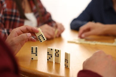 Photo of Friends playing dominoes at wooden table against light background, closeup