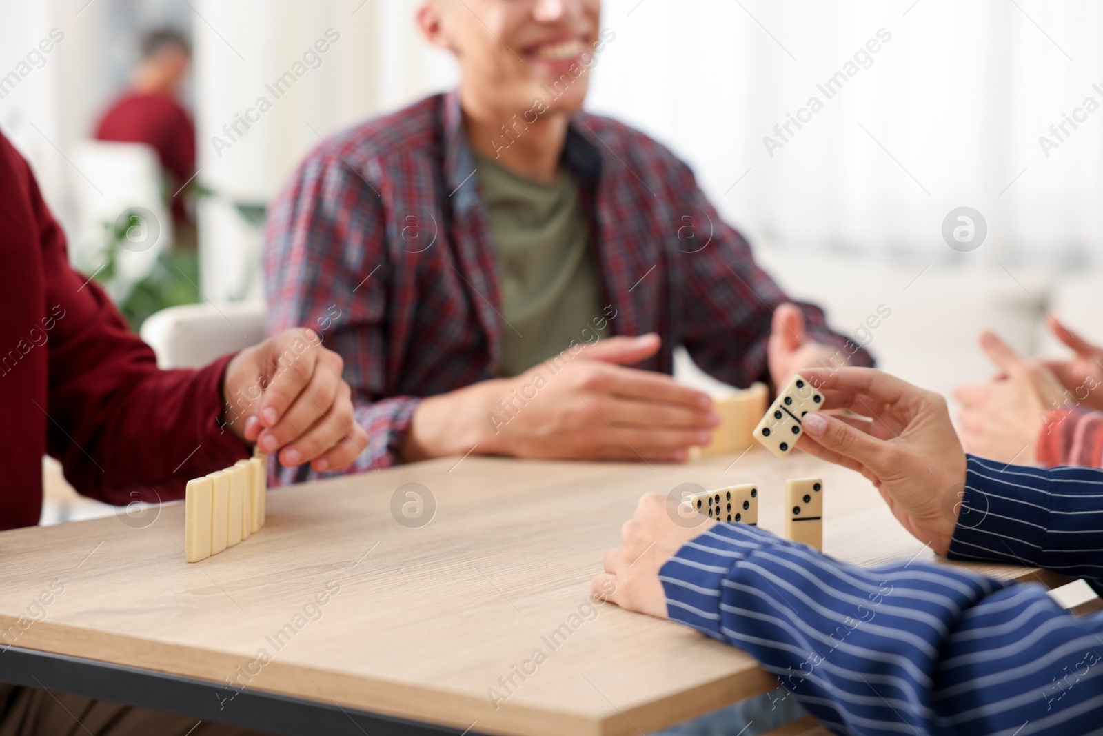Friends playing dominoes at light wooden table indoors, closeup Photo of Friends playing dominoes at light wooden table indoors, closeup