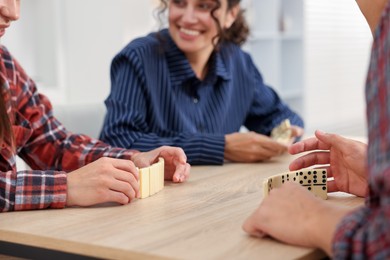 Photo of Friends playing dominoes at light wooden table indoors, closeup