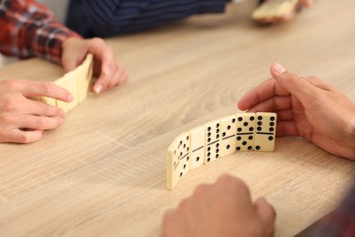 Photo of Friends playing dominoes at light wooden table, closeup