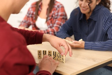 Photo of Friends playing dominoes at wooden table against light background, closeup