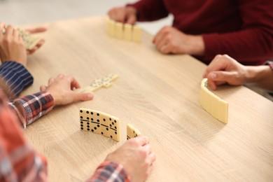 Photo of Friends playing dominoes at light wooden table, closeup