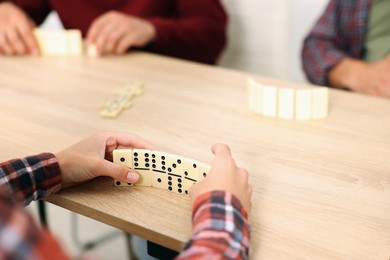 Photo of Friends playing dominoes at light wooden table, closeup