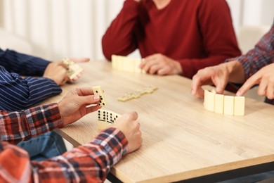 Photo of Friends playing dominoes at light wooden table indoors, closeup