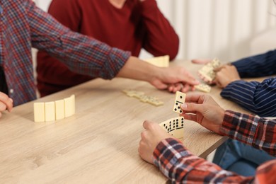 Photo of Friends playing dominoes at light wooden table indoors, closeup