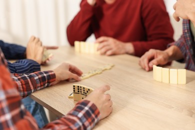 Photo of Friends playing dominoes at light wooden table indoors, closeup