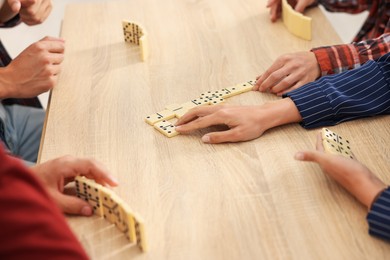 Photo of Friends playing dominoes at light wooden table, closeup
