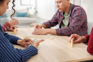 Photo of Friends playing dominoes at light wooden table indoors, closeup
