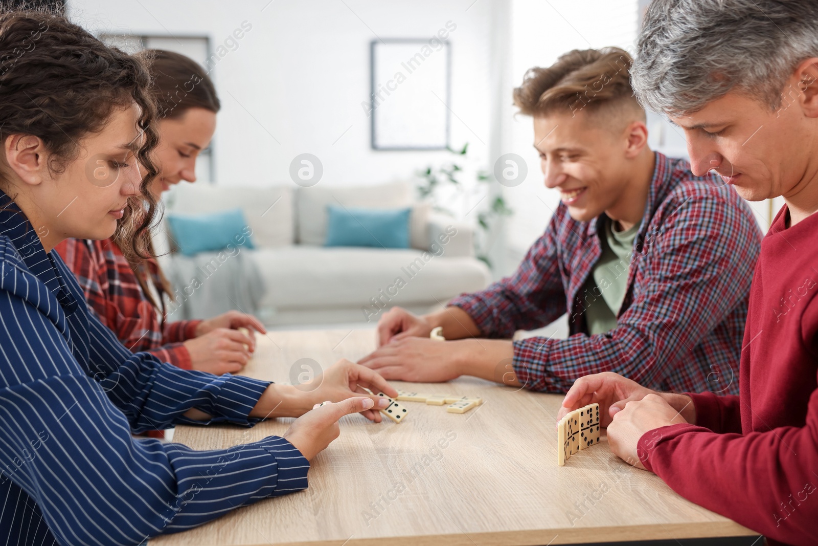 Friends playing dominoes at light wooden table indoors Photo of Friends playing dominoes at light wooden table indoors