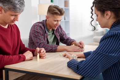 Photo of Friends playing dominoes at light wooden table indoors