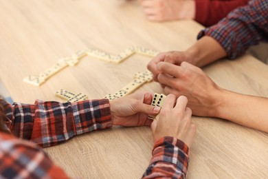 Photo of Friends playing dominoes at light wooden table, closeup