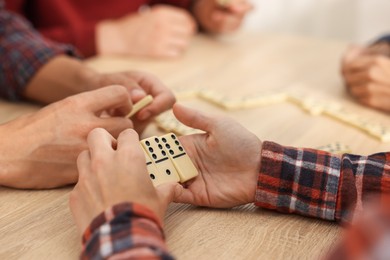 Photo of Friends playing dominoes at light wooden table, closeup