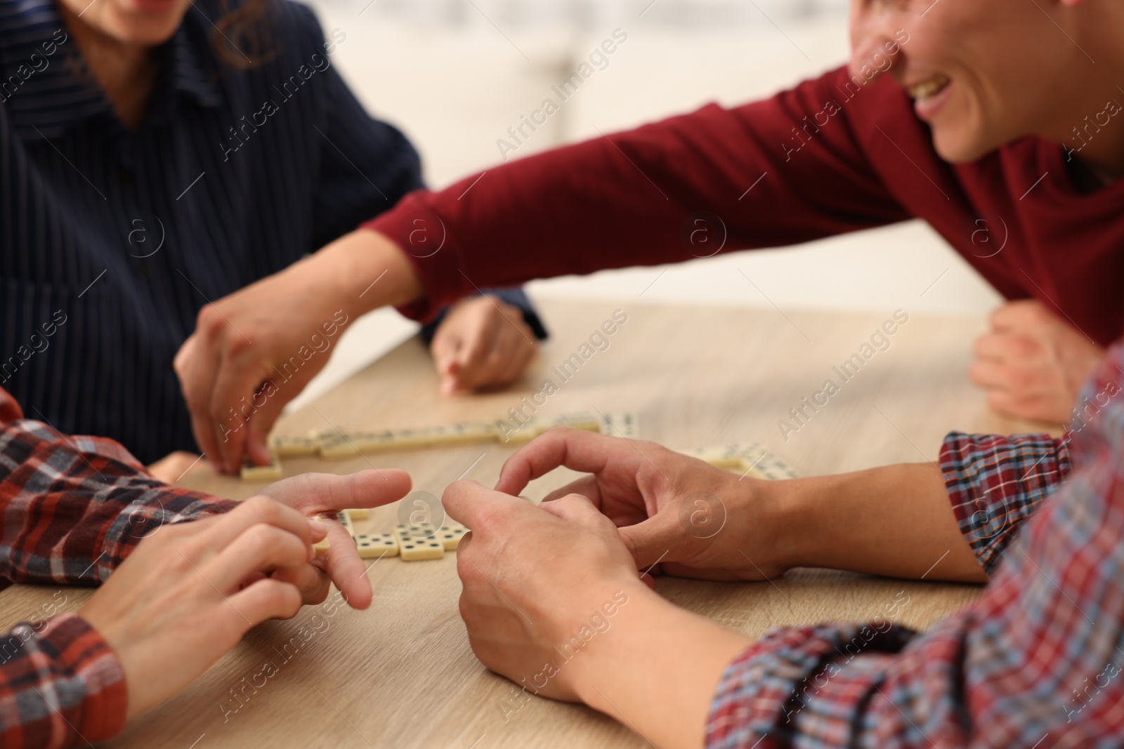 Friends playing dominoes at wooden table against light background, closeup Photo of Friends playing dominoes at wooden table against light background, closeup