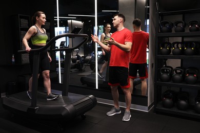 Photo of Young woman exercising on treadmill with professional personal trainer in gym