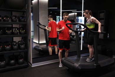 Photo of Young woman exercising on treadmill with professional personal trainer in gym