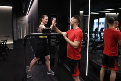 Photo of Young woman exercising on treadmill with professional personal trainer and giving high five in gym