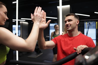 Photo of Young woman exercising on treadmill with professional personal trainer and giving high five in gym