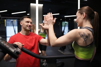 Photo of Young woman exercising on treadmill with professional personal trainer and giving high five in gym