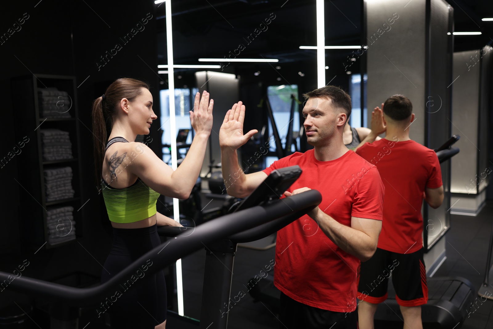 Young woman exercising on treadmill with professional personal trainer and giving high five in gym Photo of Young woman exercising on treadmill with professional personal trainer and giving high five in gym