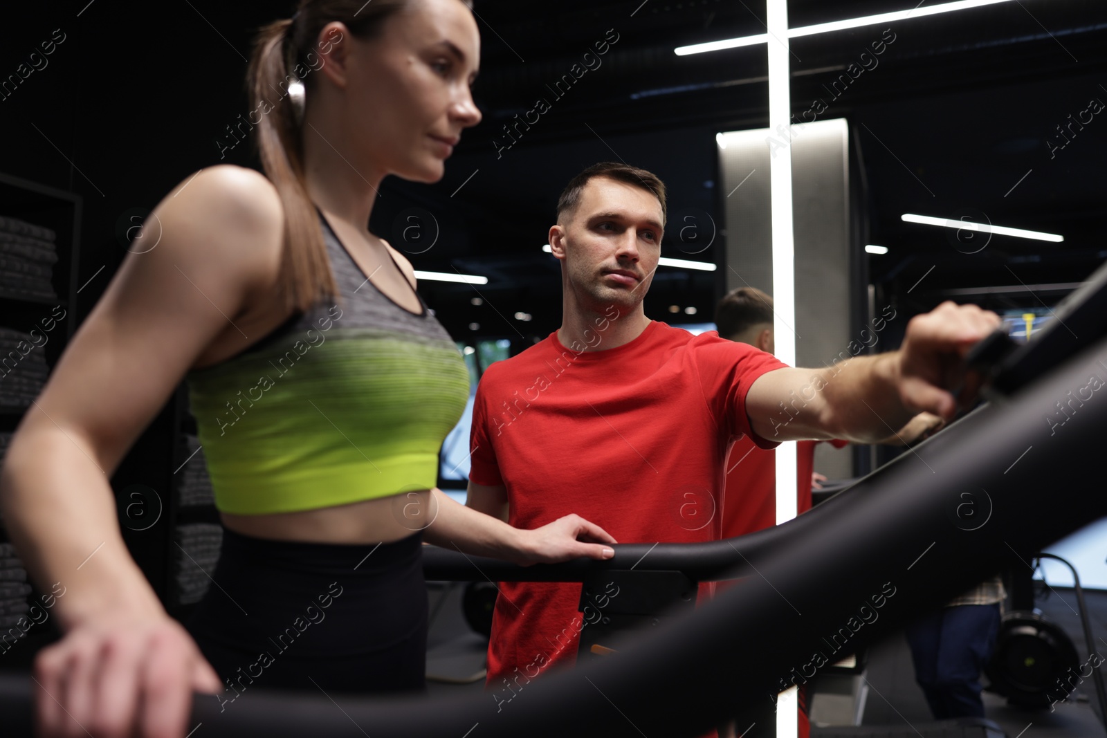 Young woman exercising on treadmill with professional personal trainer in gym Photo of Young woman exercising on treadmill with professional personal trainer in gym