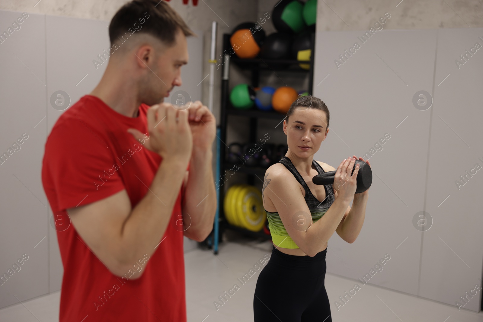 Young woman exercising with kettlebell with professional personal trainer in gym, selective focus Photo of Young woman exercising with kettlebell with professional personal trainer in gym, selective focus
