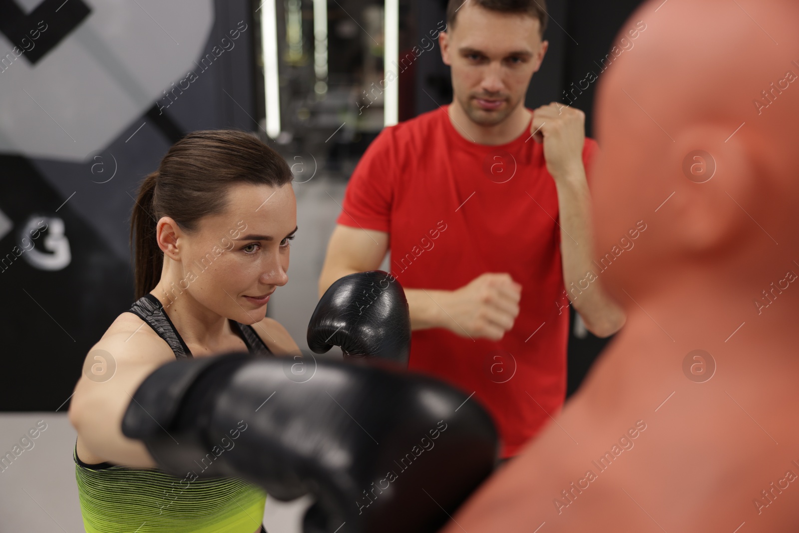 Young woman exercising with punching dummy with professional personal trainer in gym Photo of Young woman exercising with punching dummy with professional personal trainer in gym
