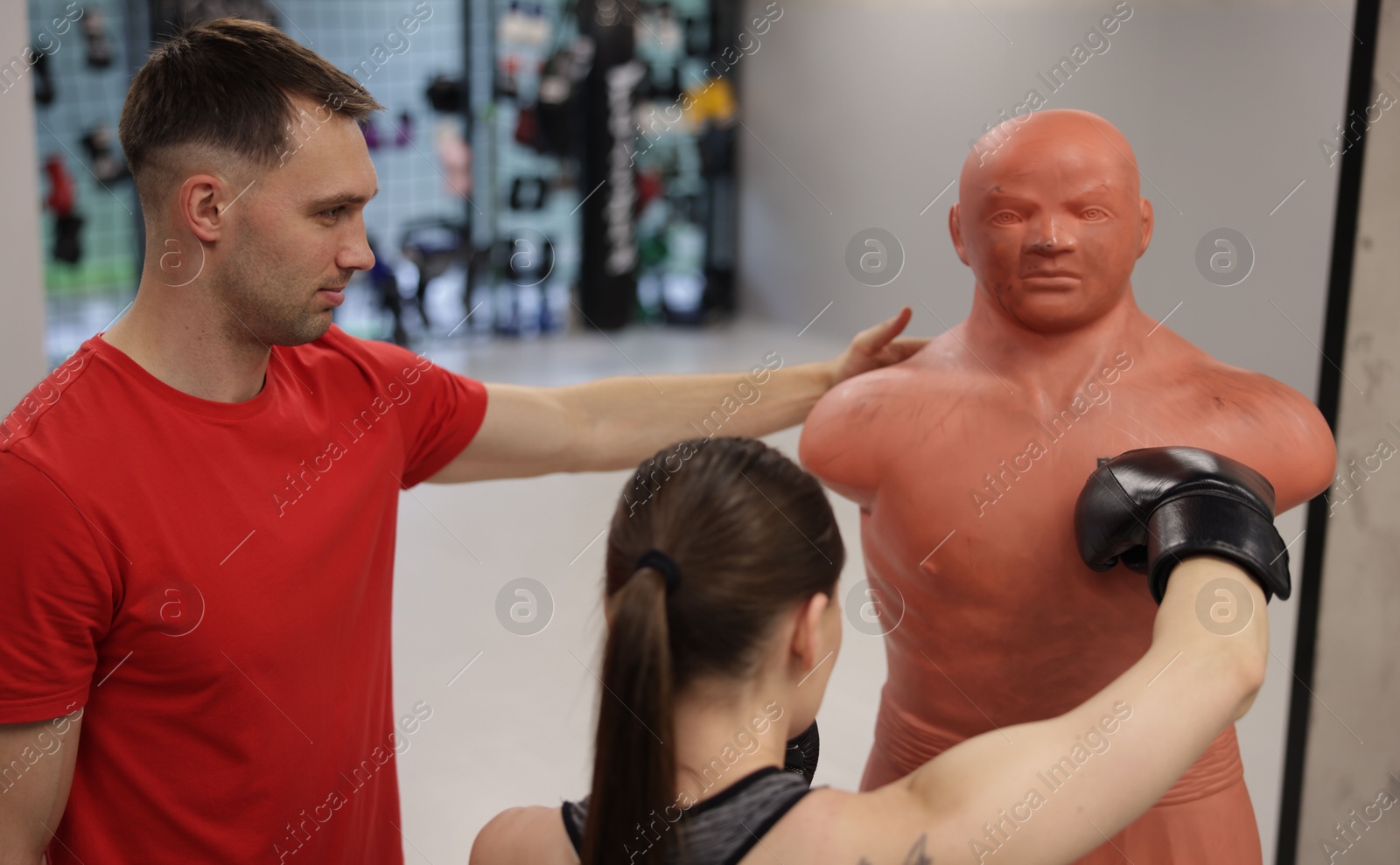 Young woman exercising with punching dummy with professional personal trainer in gym Photo of Young woman exercising with punching dummy with professional personal trainer in gym