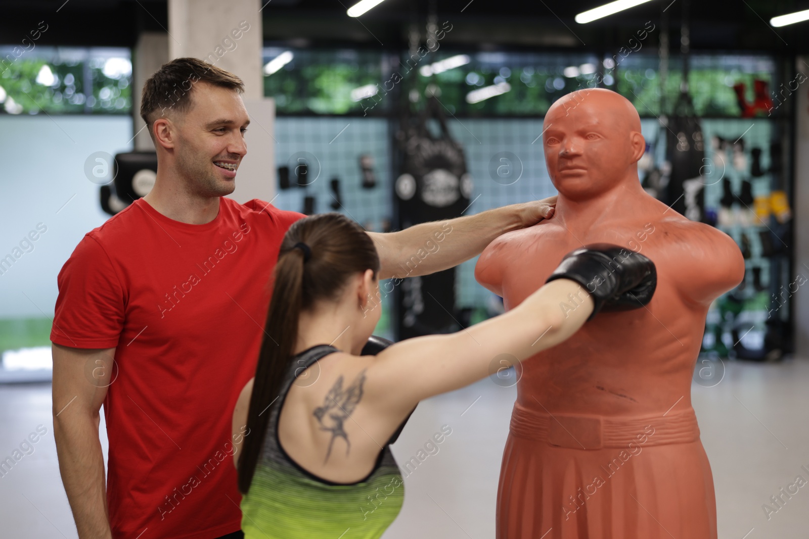 Young woman exercising with punching dummy with professional personal trainer in gym Photo of Young woman exercising with punching dummy with professional personal trainer in gym