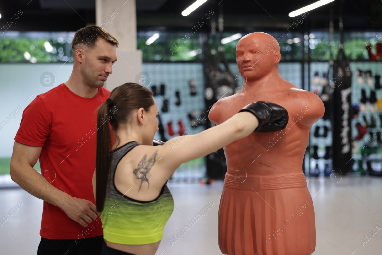Young woman exercising with punching dummy with professional personal trainer in gym Photo of Young woman exercising with punching dummy with professional personal trainer in gym