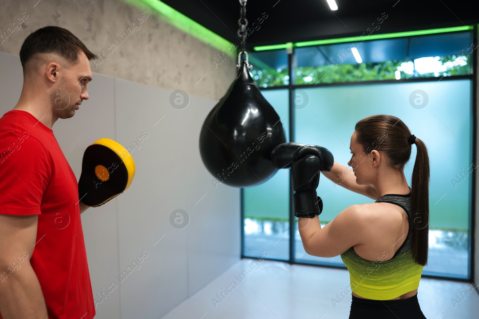 Young woman exercising with punching bag with professional personal trainer in gym Photo of Young woman exercising with punching bag with professional personal trainer in gym