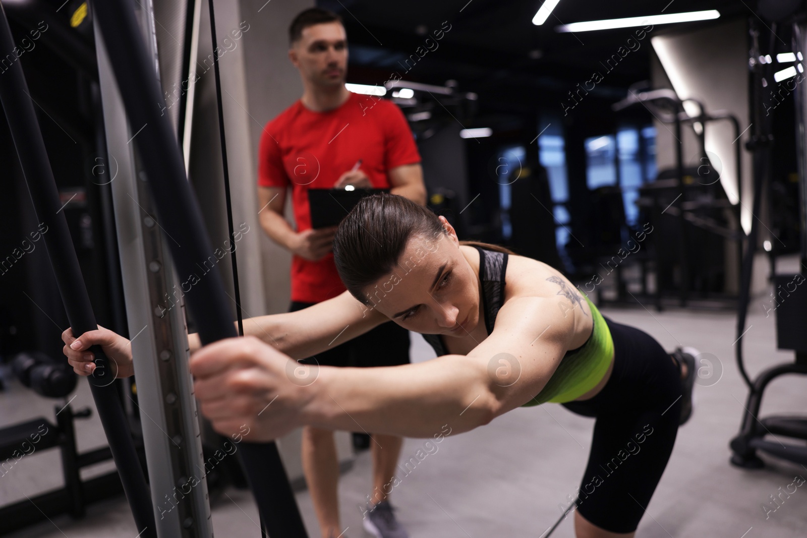 Young woman exercising with cable machine with professional personal trainer in gym Photo of Young woman exercising with cable machine with professional personal trainer in gym