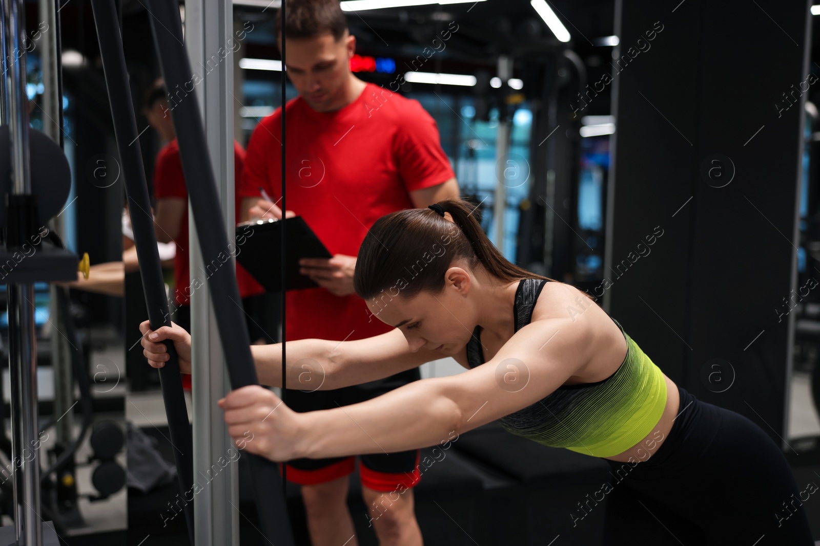 Young woman exercising with cable machine with professional personal trainer in gym Photo of Young woman exercising with cable machine with professional personal trainer in gym