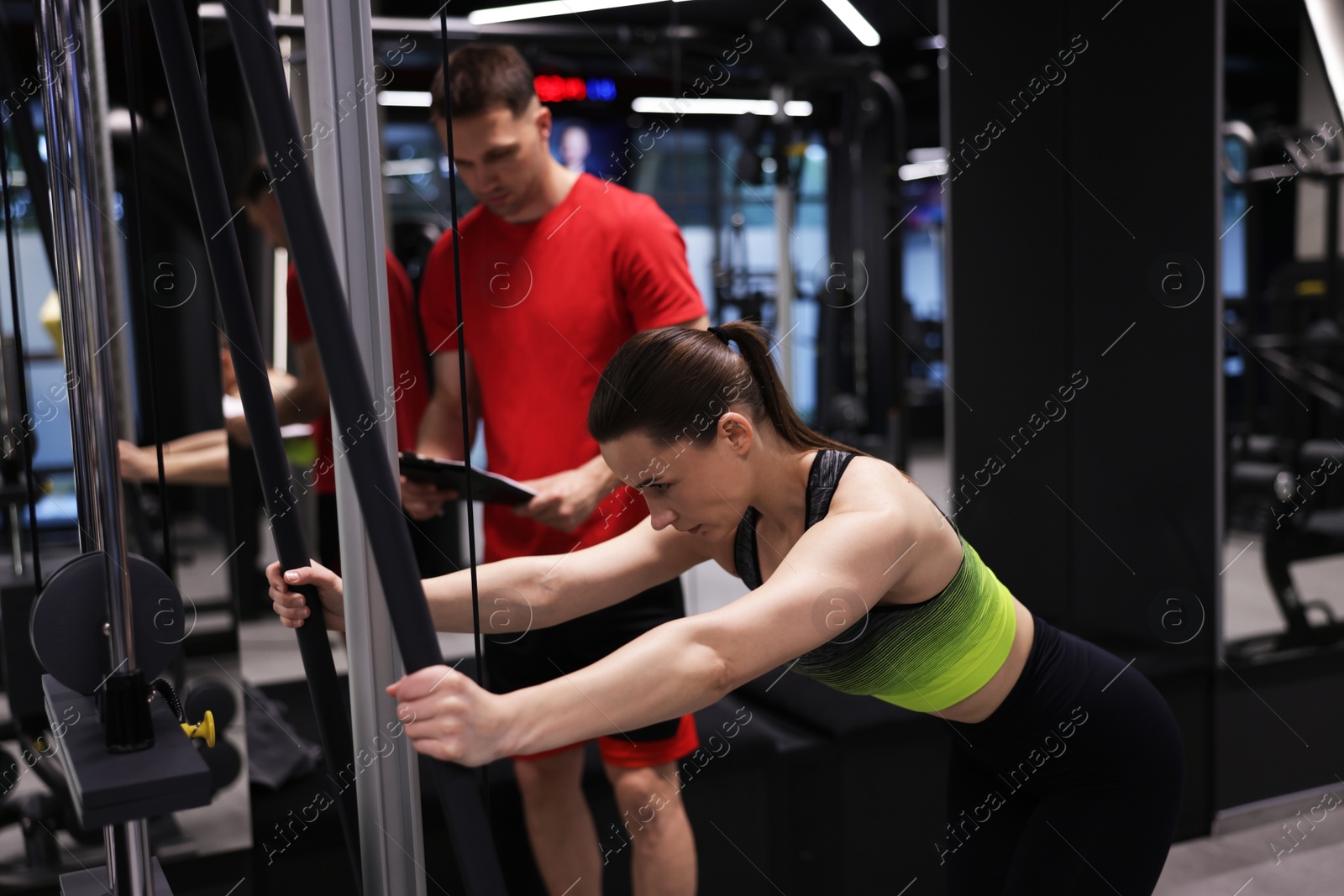Young woman exercising with cable machine with professional personal trainer in gym Photo of Young woman exercising with cable machine with professional personal trainer in gym