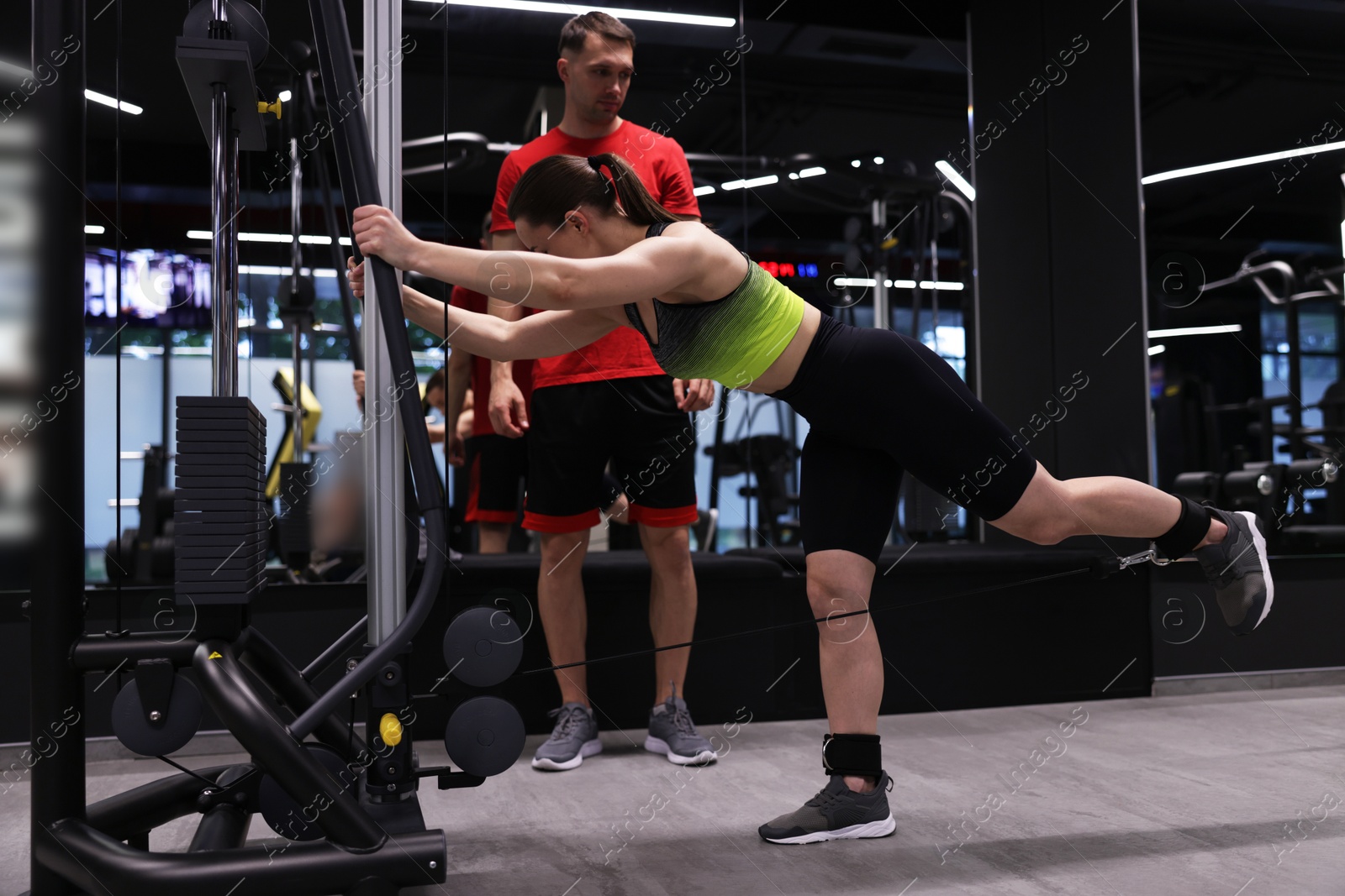 Young woman exercising with cable machine with professional personal trainer in gym Photo of Young woman exercising with cable machine with professional personal trainer in gym