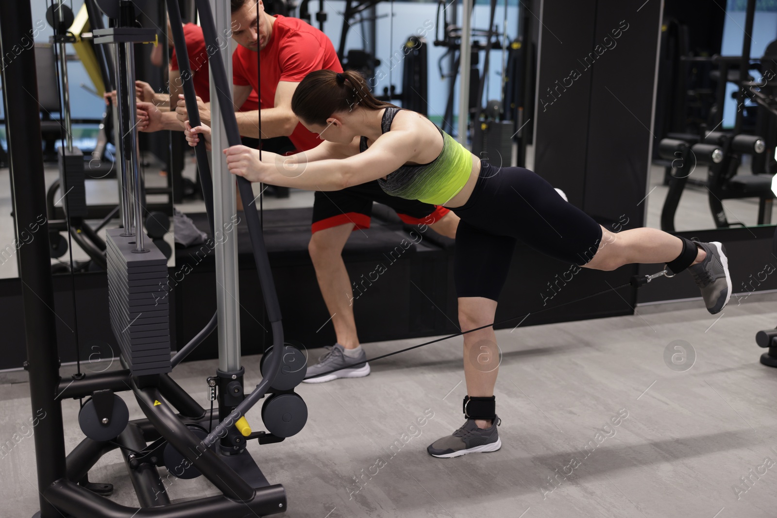 Young woman exercising with cable machine with professional personal trainer in gym Photo of Young woman exercising with cable machine with professional personal trainer in gym
