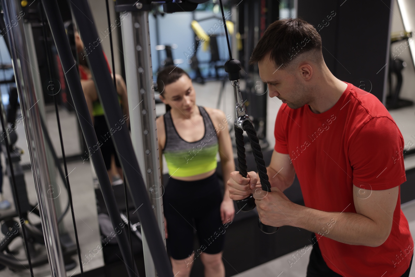 Professional personal trainer showing young woman how to exercise with lat pulldown machine in gym Photo of Professional personal trainer showing young woman how to exercise with lat pulldown machine in gym