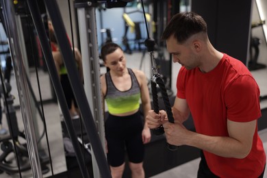 Photo of Professional personal trainer showing young woman how to exercise with lat pulldown machine in gym