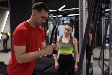 Photo of Professional personal trainer showing young woman how to exercise with lat pulldown machine in gym