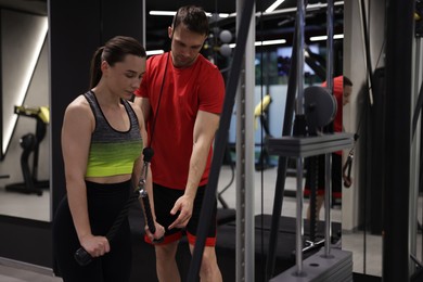 Photo of Young woman exercising with lat pulldown machine with professional personal trainer in gym