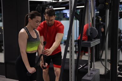 Photo of Young woman exercising with lat pulldown machine with professional personal trainer in gym