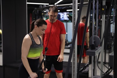 Photo of Young woman exercising with lat pulldown machine with professional personal trainer in gym