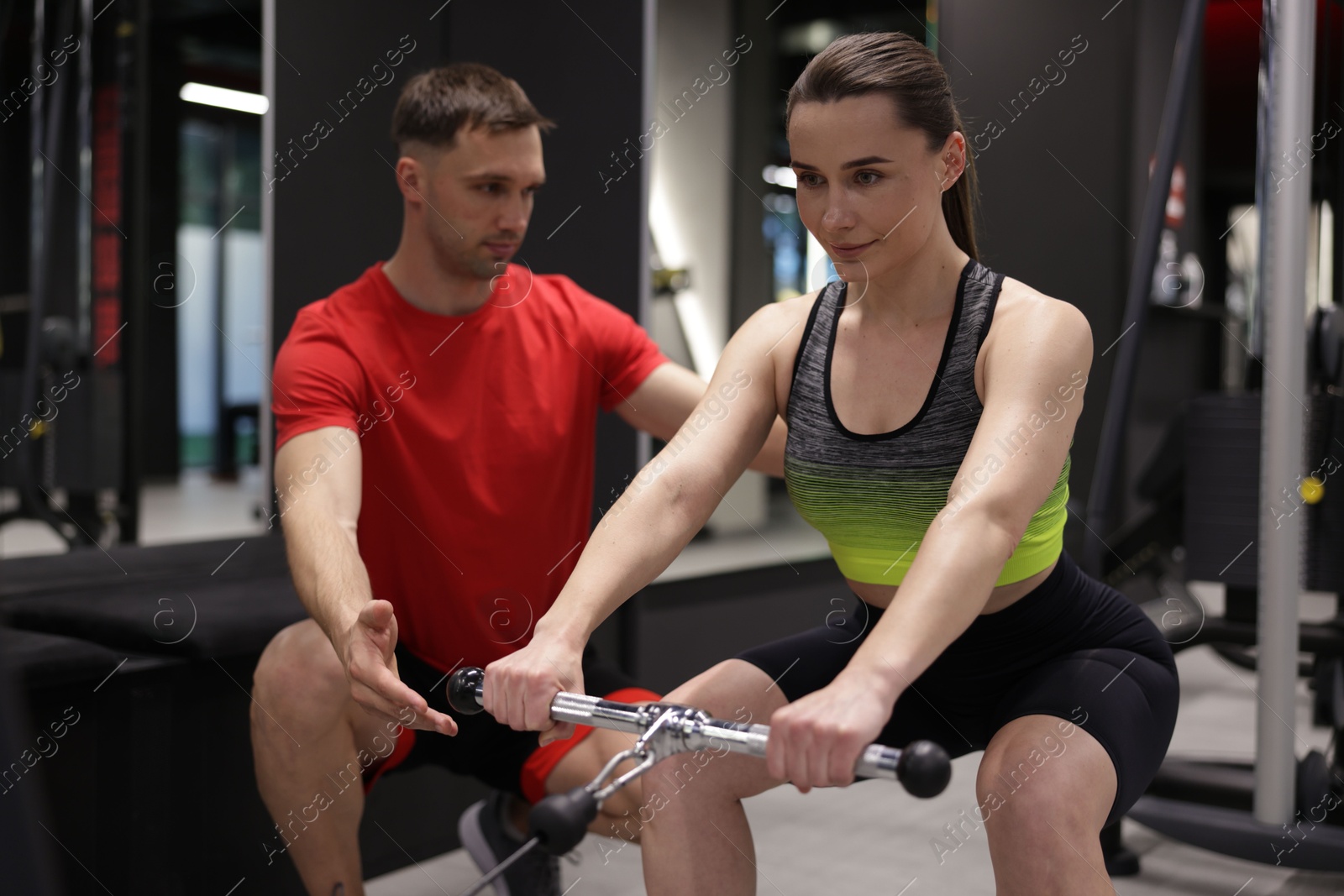 Young woman exercising with cable machine with professional personal trainer in gym Photo of Young woman exercising with cable machine with professional personal trainer in gym