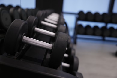 Photo of Many metal dumbbells on stand in gym, closeup