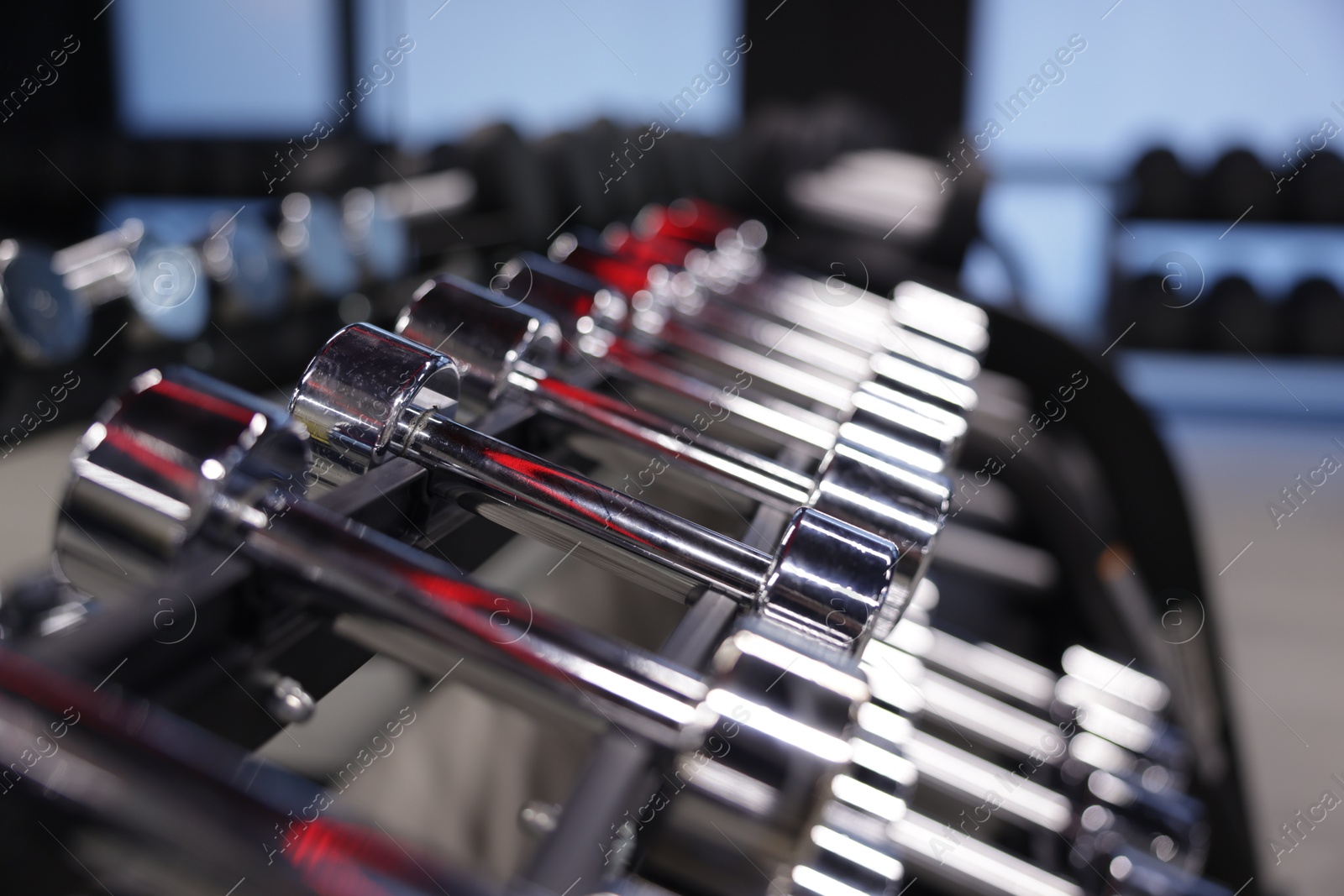 Photo of Many metal dumbbells on stand in gym, closeup