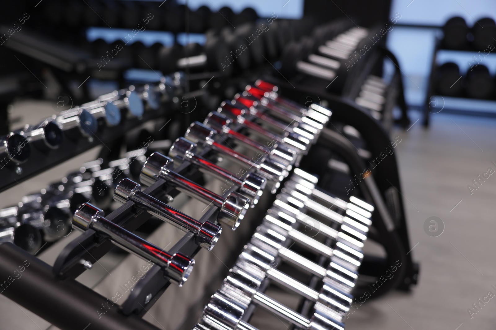 Photo of Many metal dumbbells on stand in gym, closeup