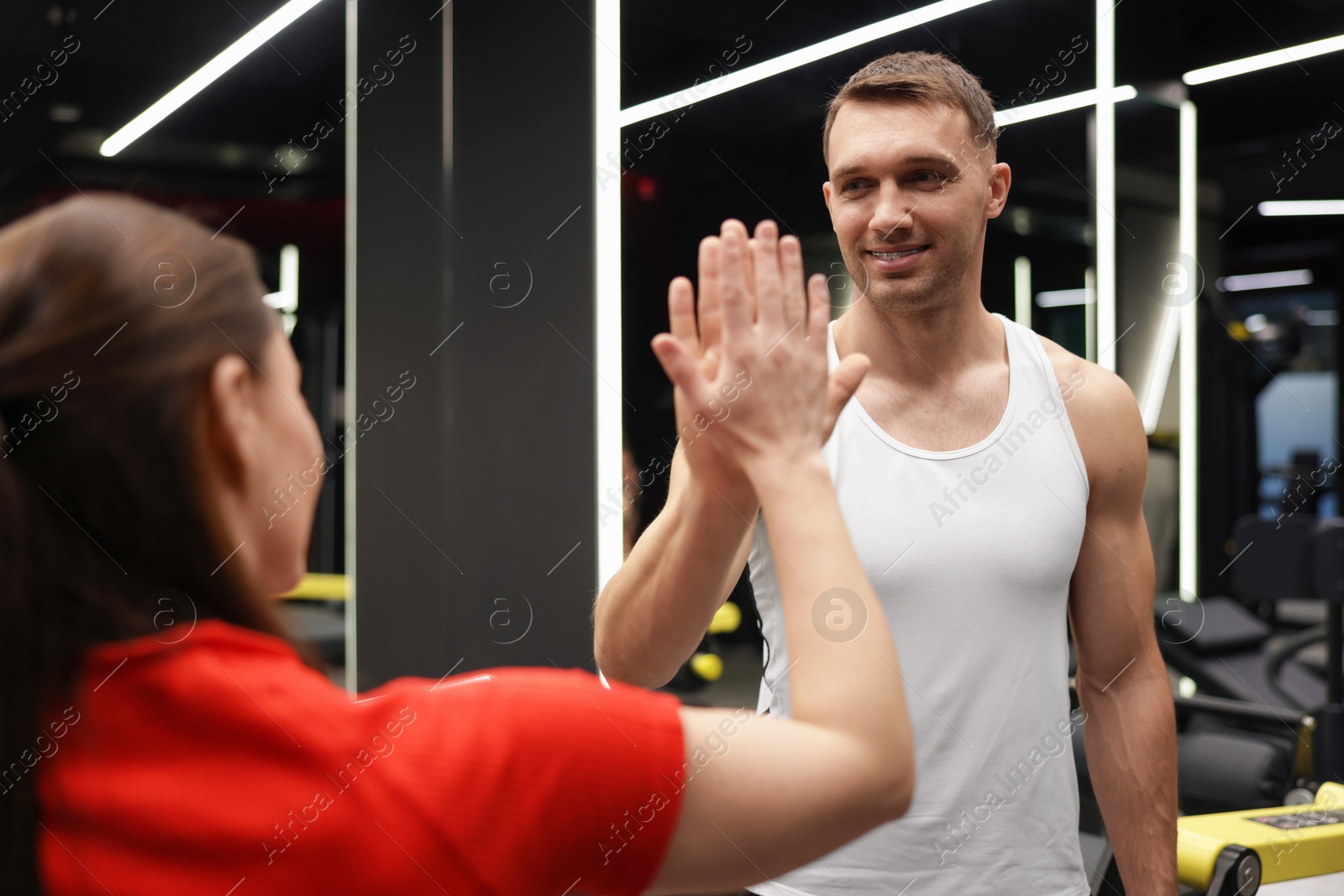 Young woman with professional personal trainer giving high five in gym Photo of Young woman with professional personal trainer giving high five in gym